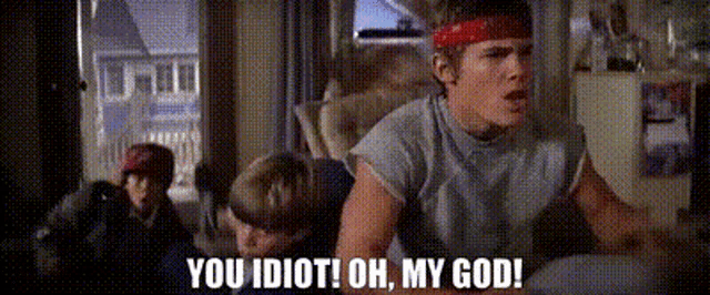 a man with a red headband is sitting in a chair and saying you idiot oh my god .