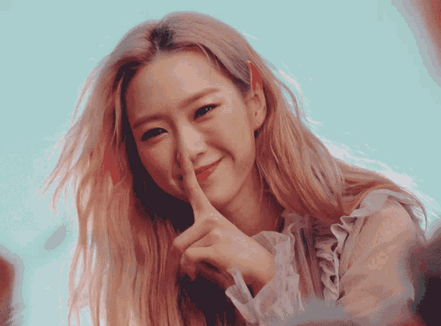 a woman with pink hair is smiling and holding her finger to her mouth