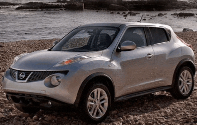 a silver nissan juke is parked on a rocky beach near water
