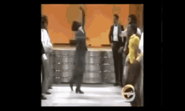 a woman in a black dress is dancing on a stage in front of a group of people .