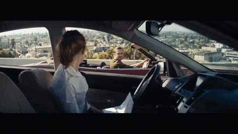 a man driving a red convertible with a woman sitting in the back seat
