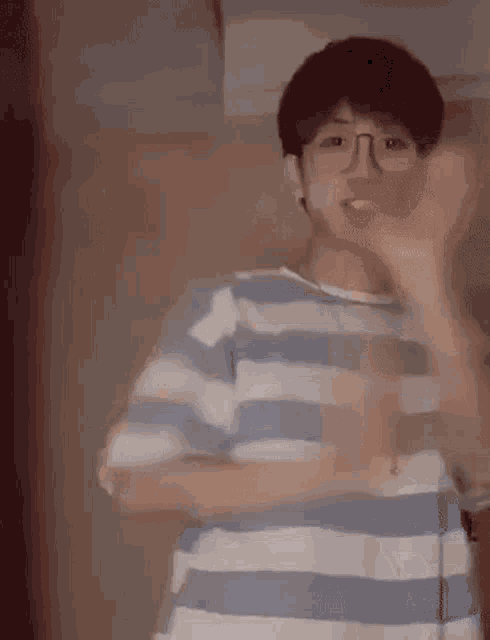 a young man wearing glasses and a blue and white striped shirt is dancing in a room .