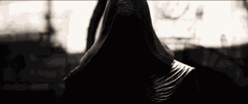 a grim reaper with a hood on his head is standing in the dark .