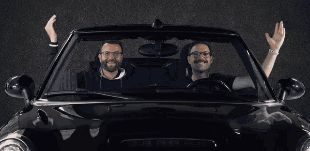 two men sitting in a car with their arms in the air