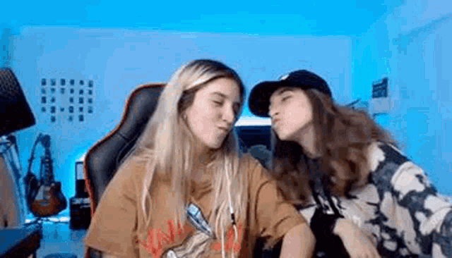 two girls are kissing each other on the cheek while sitting in front of a computer screen .