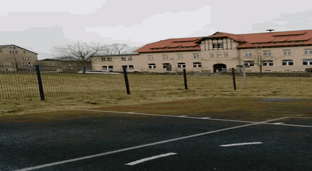 a large building with a red tile roof is behind a basketball court