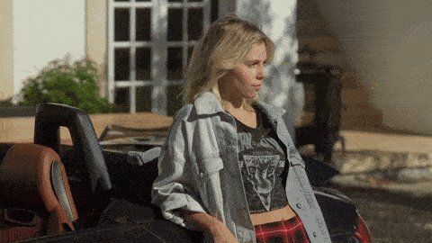 a woman in a crop top and plaid shorts is sitting in a black car