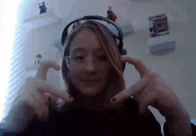a girl wearing headphones and glasses is making a heart shape with her hands