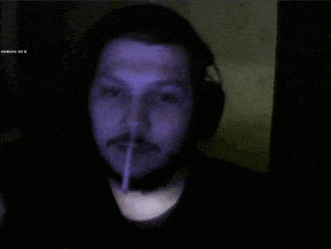 a man wearing headphones is smoking a cigarette in a dark room with a blue light behind him