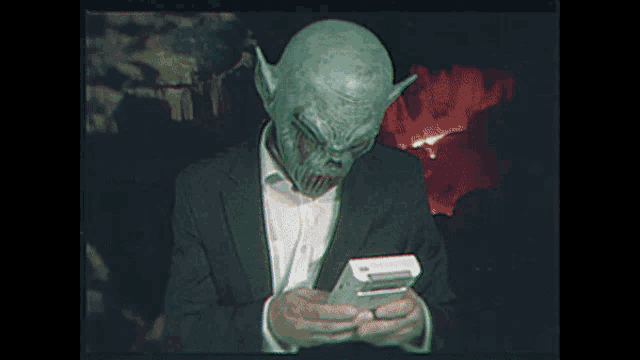 a man in a suit and tie with a green monster mask on his face