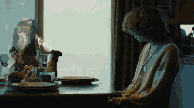a woman is sitting at a table with plates and a ghost behind her