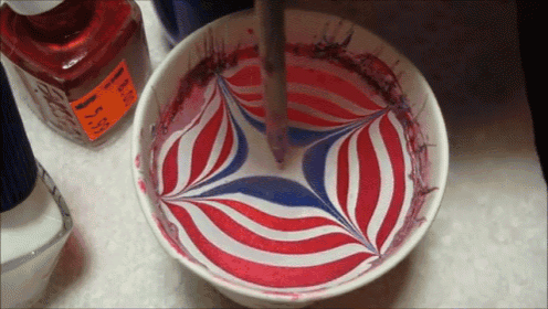 a bowl of red white and blue paint with a bottle of red ink next to it
