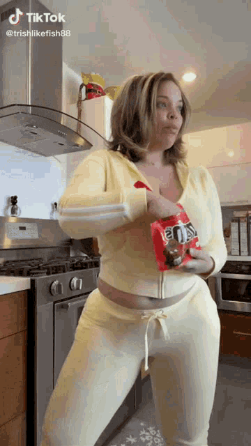a woman in a yellow tracksuit is holding a bag of candy .