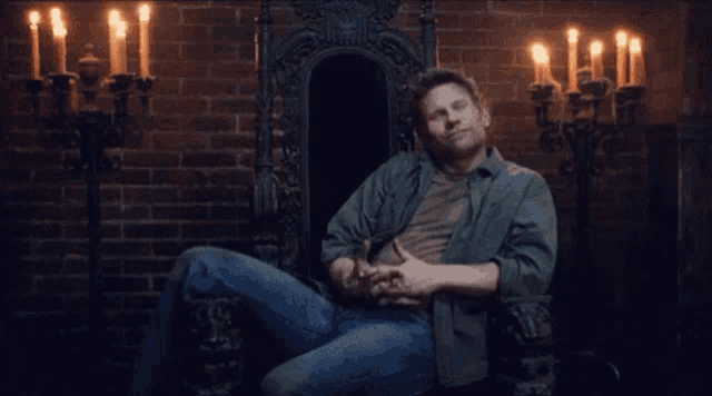a man in a green shirt is sitting in a chair with candles in the background