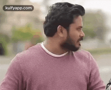 a man with a beard is wearing a pink sweater and a white shirt .