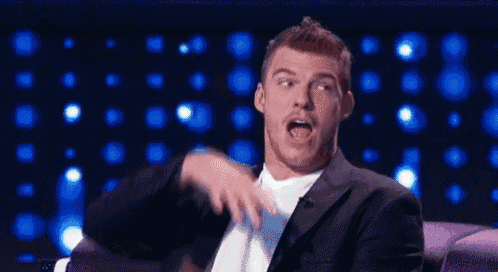 a man in a suit and tie is sitting on a couch with his mouth open .