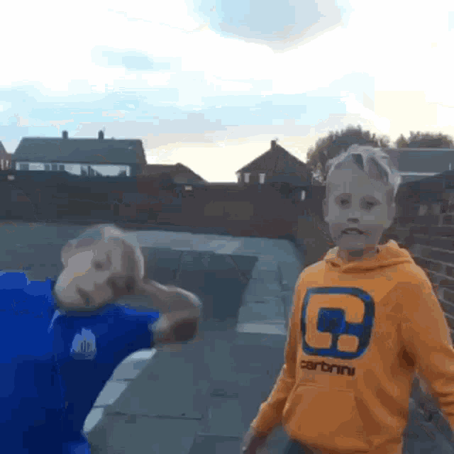 a boy wearing an orange carhartt sweatshirt stands next to another boy