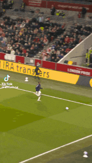 a soccer player is kicking a ball on a field with a banner for ira transfers behind him