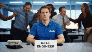 a man sitting at a desk with a sign that says data engineer on it