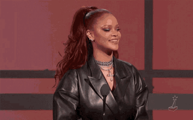 a woman in a leather jacket is standing in front of a microphone and waving .