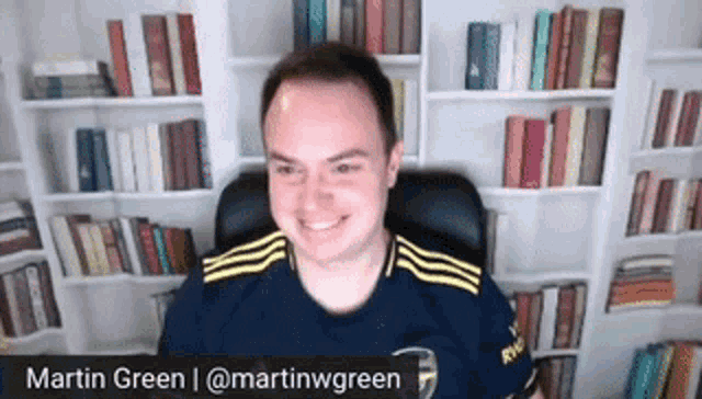 a man in a blue shirt is smiling in front of a bookshelf
