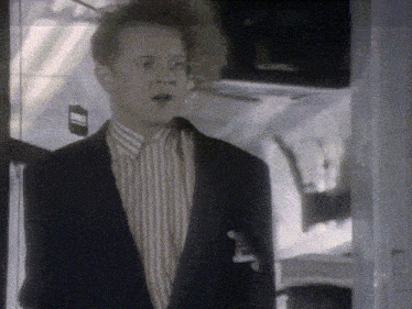 a man in a suit and striped shirt is standing in front of a sign that says ' emergency exit '