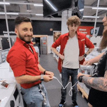 a man in a red shirt stands next to two other men in a store