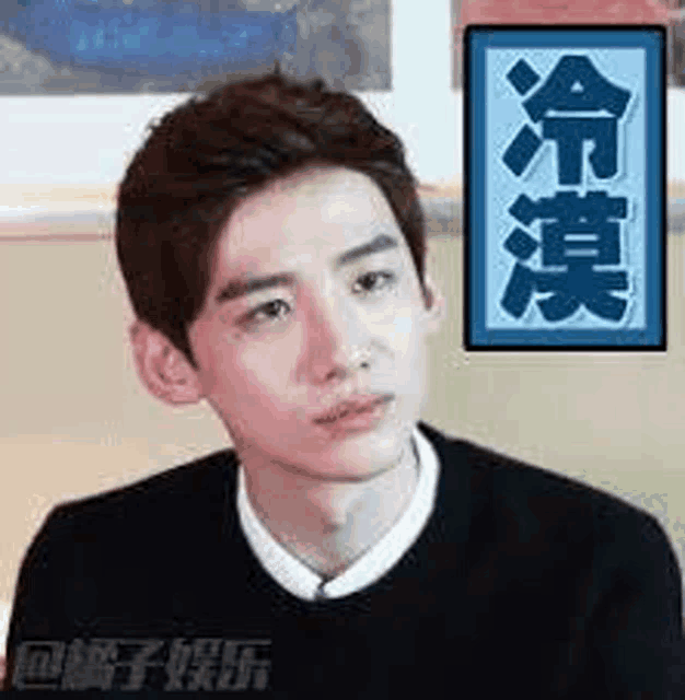 a young man in a black sweater and white shirt is sitting in front of a wall .