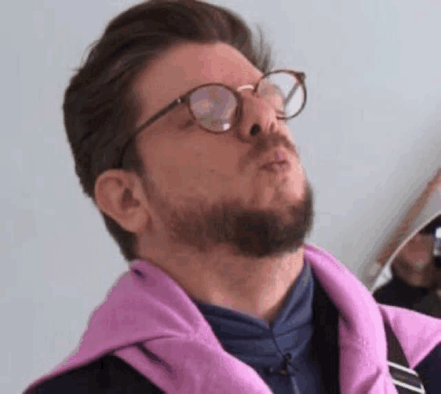 a man with a beard and glasses is wearing a pink jacket and making a funny face .