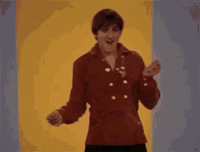 a man in a red jacket is dancing in front of a yellow wall .