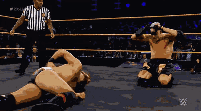 a wrestler is kneeling down in a wrestling ring with a referee in the background