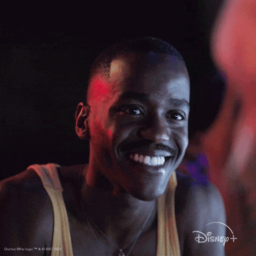 a man is smiling in front of a disney + logo