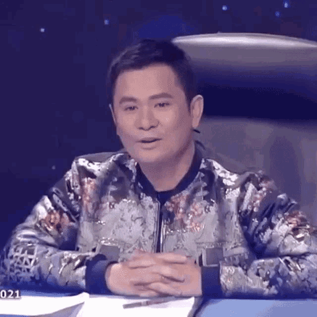 a man is sitting at a table with his hands folded and looking at the camera .