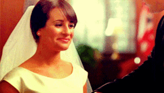 a woman in a wedding dress and veil is smiling while standing next to a man