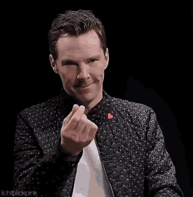 a man in a jacket is making a heart shape with his fingers .