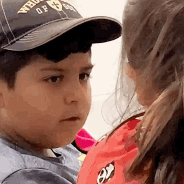 a little boy wearing a hat is looking at a little girl wearing a red shirt .