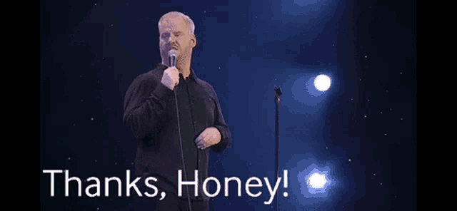 a man is standing in front of a microphone on a stage and saying `` thanks , honey ! ''