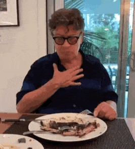 a man wearing glasses is sitting at a table with a plate of food .