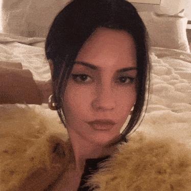 a woman wearing a fur coat and hoop earrings is laying on a bed