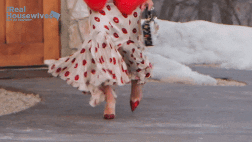 a woman wearing a red and white polka dot skirt is walking in front of a real housewives sign