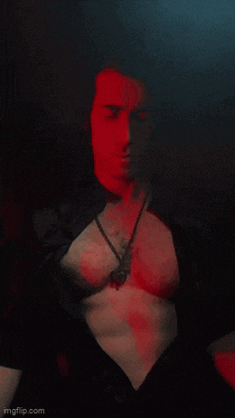 a shirtless man with a necklace around his neck is standing in a dark room .