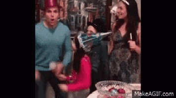 a group of people are standing around a table with a girl wearing a party hat on her head .