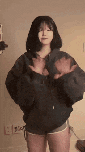 a woman in a black jacket and shorts is dancing in front of a camera .