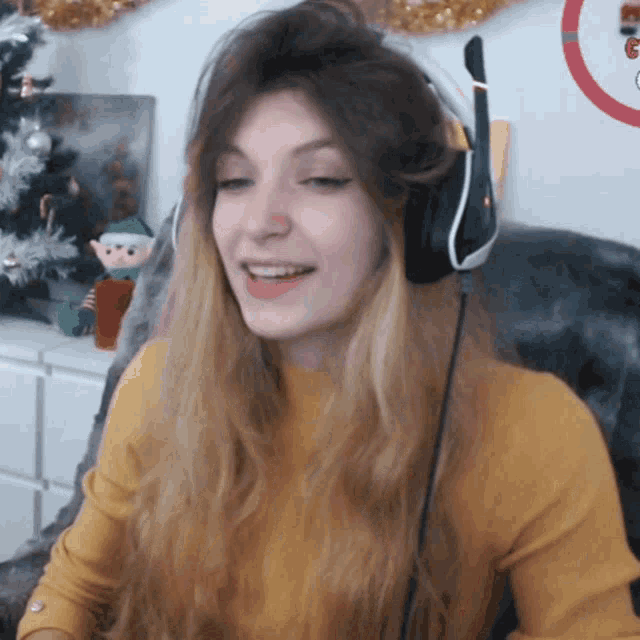 a woman wearing headphones and a yellow sweater is smiling in front of a christmas tree