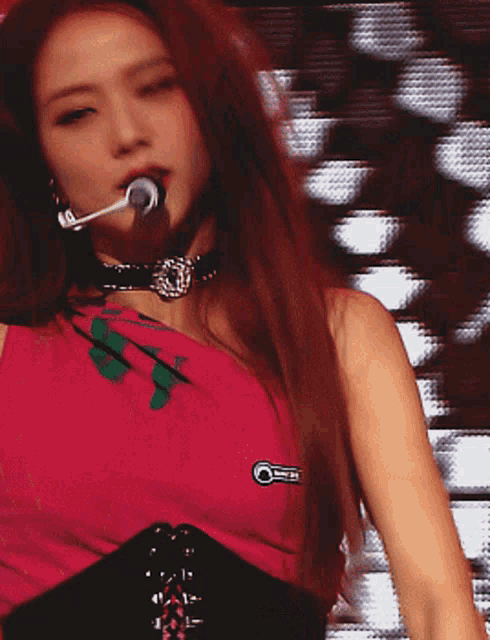 a woman singing into a microphone wearing a choker and a pink shirt