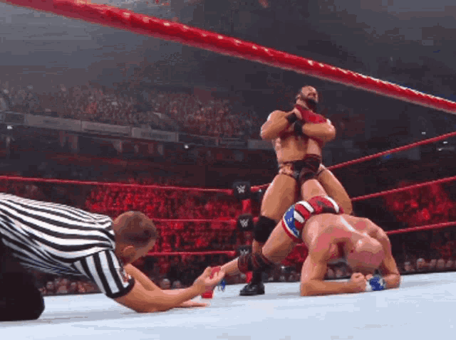a referee is kneeling down in front of two wrestlers in a wrestling match
