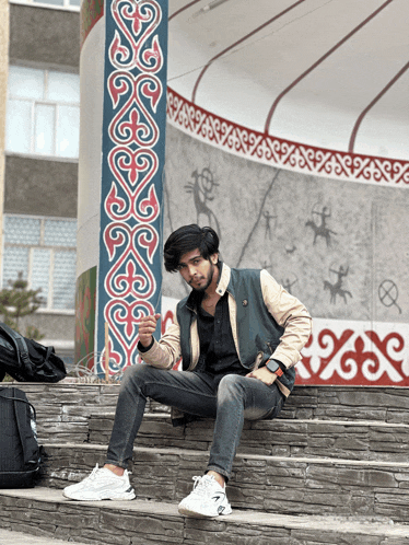 a young man sits on a set of stone steps in front of a wall that has a pattern of swirls