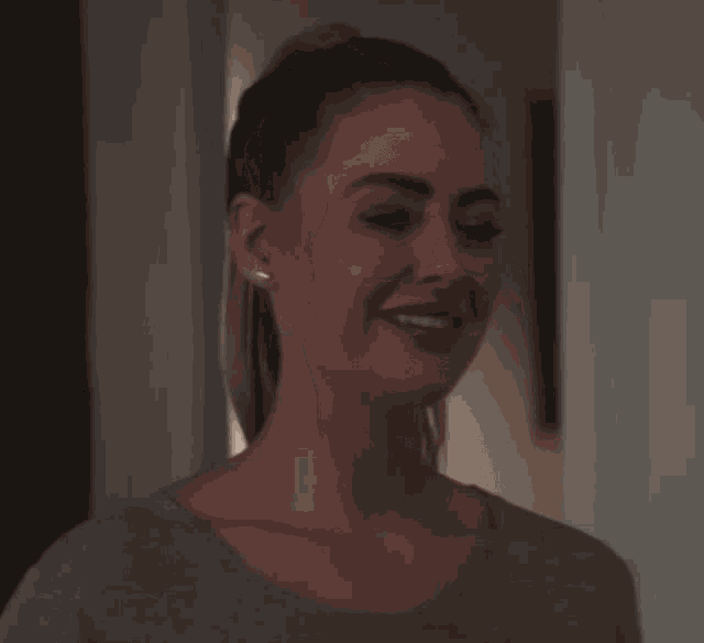 a woman with a ponytail is smiling and wearing a grey shirt