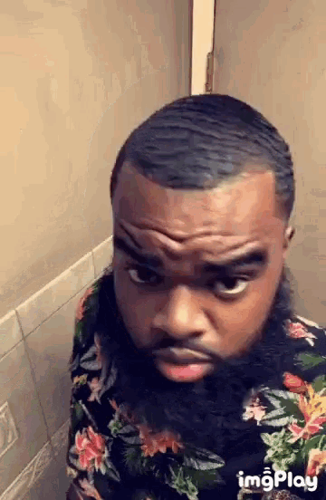 a man with a beard is making a funny face while sitting in a bathroom .