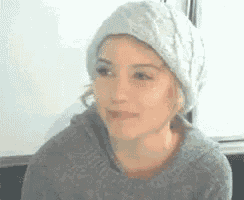 a woman wearing a gray sweater and a white hat is looking to the side .